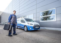 Un employé de Blueserv avec une boîte à outils devant une voiture Blueserv de marque